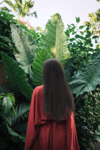 about woman facing away from camera with long hair in garden with tropical green plants